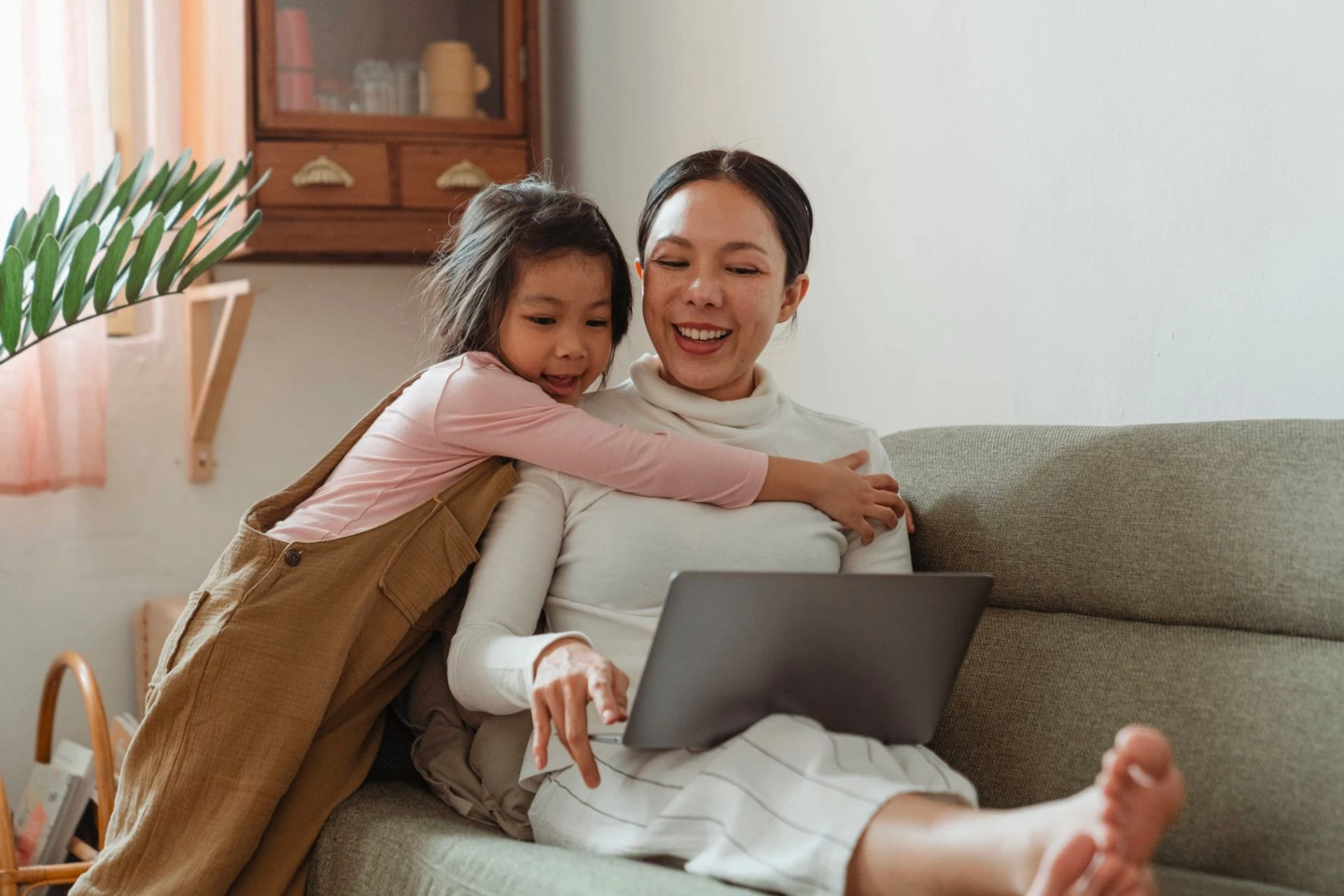 Woman and girl hugging on a sofa next to a laptop