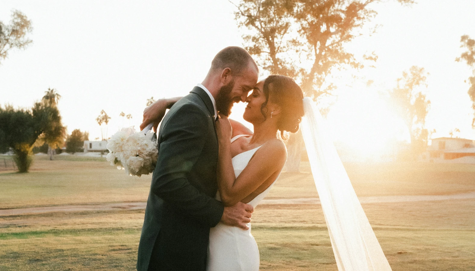 Bride and groom kissing in a sunlit field on their wedding day