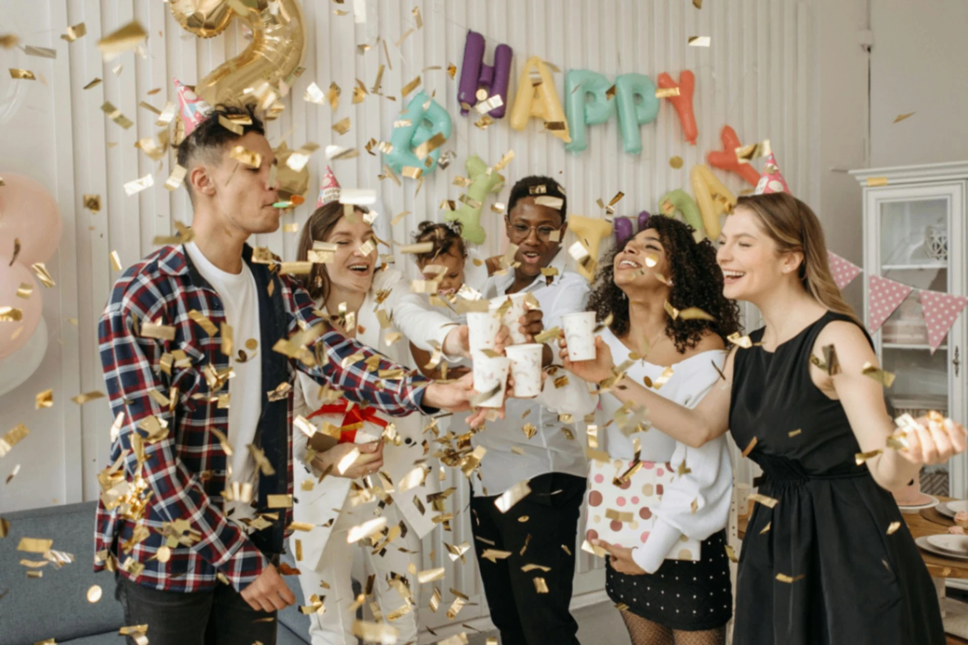 Friends toasting at a birthday party with confetti and balloons